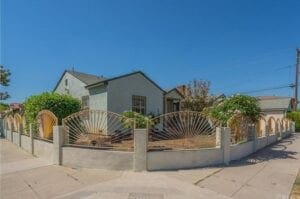 A house with a fence and palm trees in front of it.